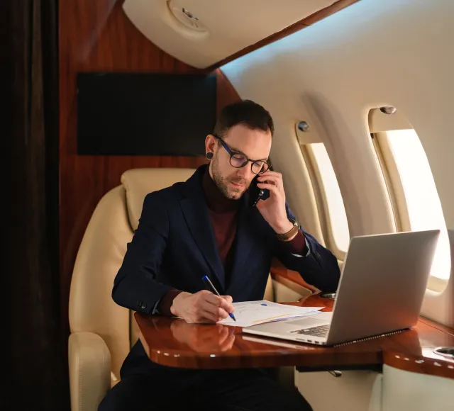 A private jet passenger uses their laptop and phone on board.