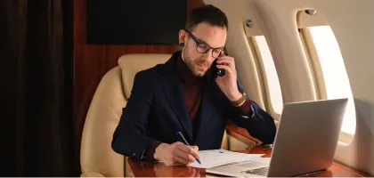Photo of a businessman using his laptop and mobile while on the plane