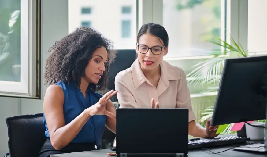 Image of two women talking next to a laptop