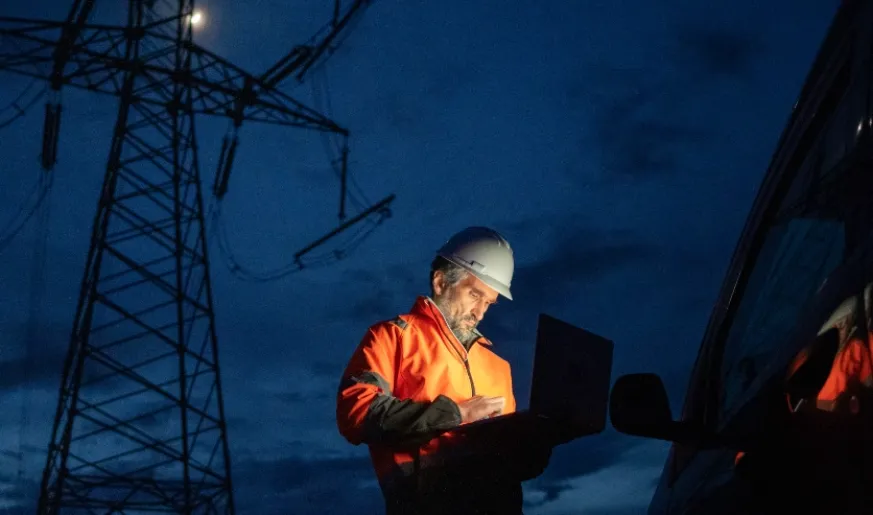 Photo of an engineer working on his laptop during the night on an industrial site