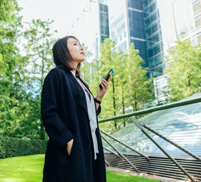 Photo of a woman standing in a park with a phone in her hand while looking up