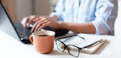 Photo of someone typing on their laptop in an office with documents next to them
