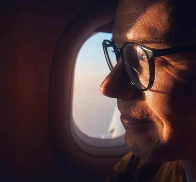 Photo of a man with glasses sitting on a plane staring outside the window