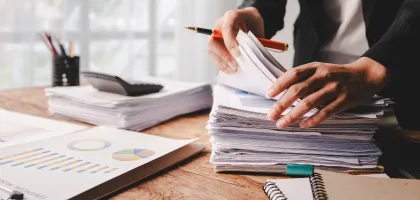 Photo of a desk with laptop, documents and a person by the desk