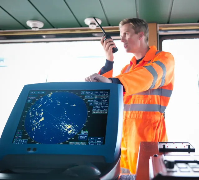 Photo of a man standing on a Ship Deck talking into the radio