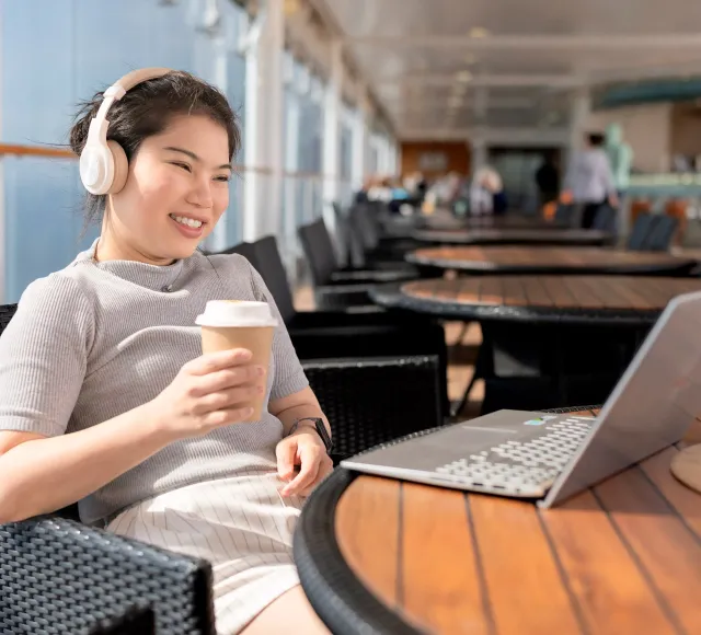 Photo of a female passenger on a ferry using her laptop with headset