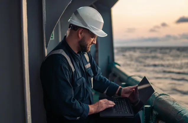 Photo of a maritime worker on deck with a laptop