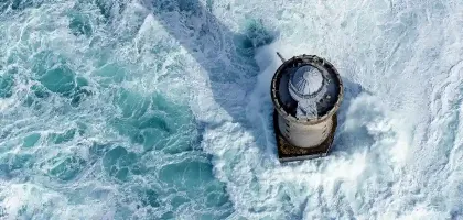 Aerial view of the Créac’h Lighthouse during a storm, with strong waves and rough seas.