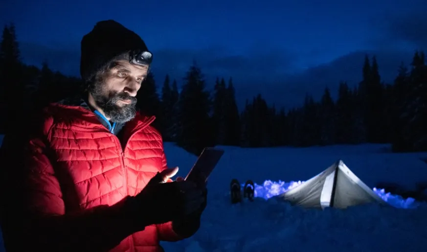 Photo of a man using a tablet while camping during winter