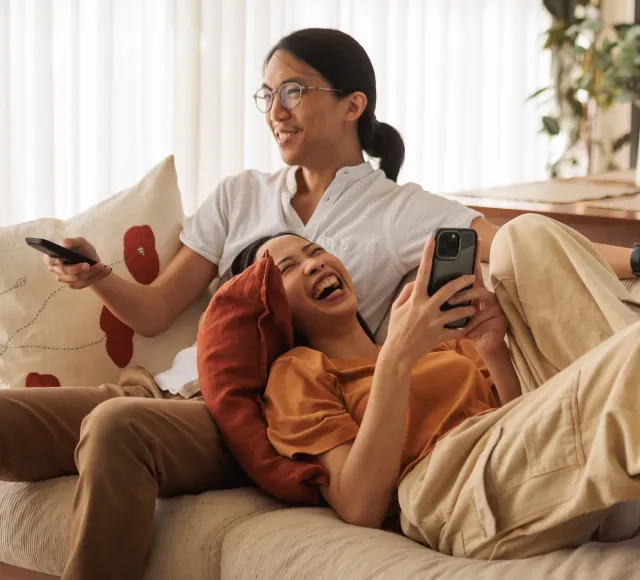 Photo of a young couple using their phone and watching the TV smiling