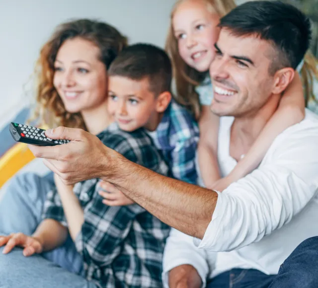 Photo of a family smiling and watching television 