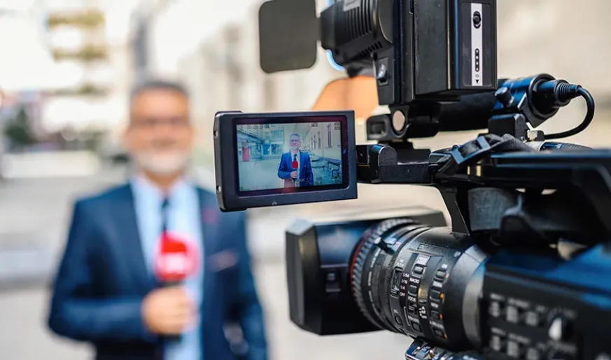 Photo of a camera filming journalist