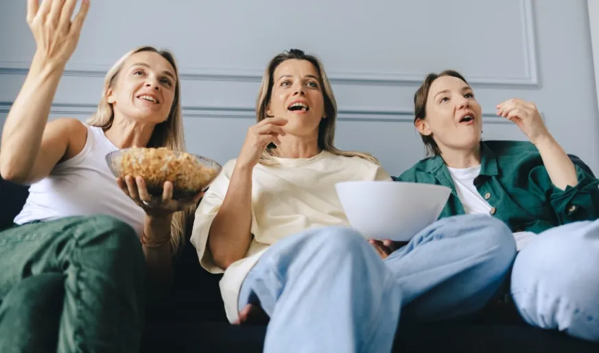 Photo of three women watching TV while eating popcorn