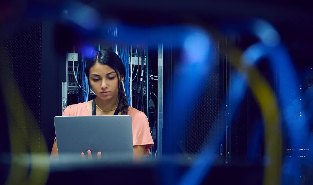 Image of a woman working on her laptop in a server room